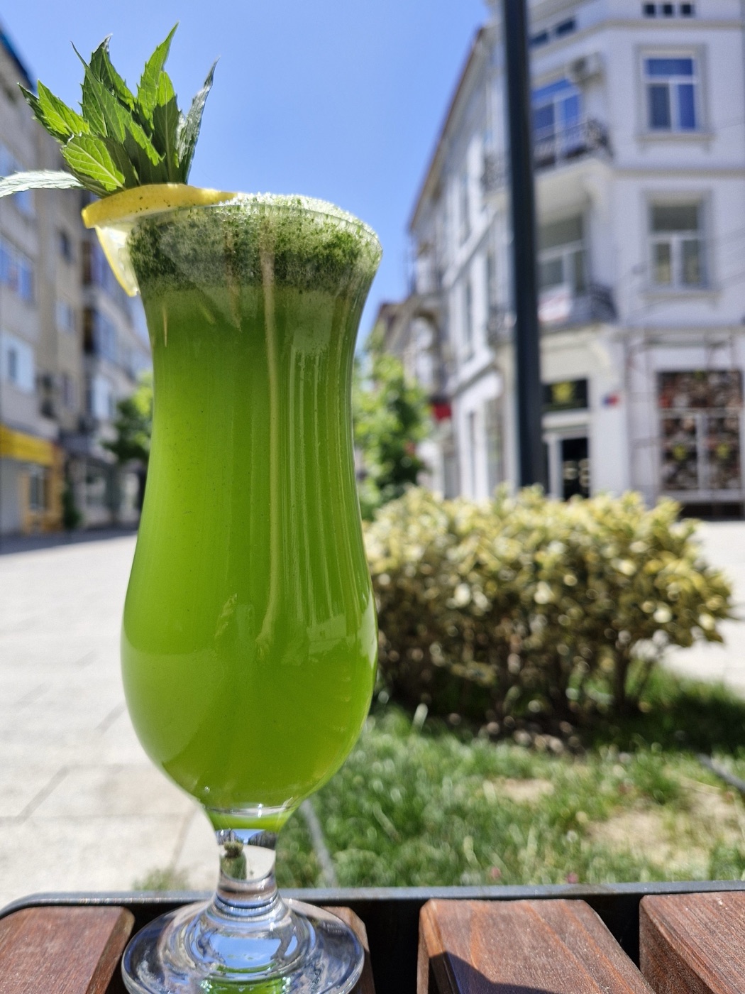 Băutură verde cu mentă și lămâie într-un pahar înalt, afară, pe o bancă de lemn